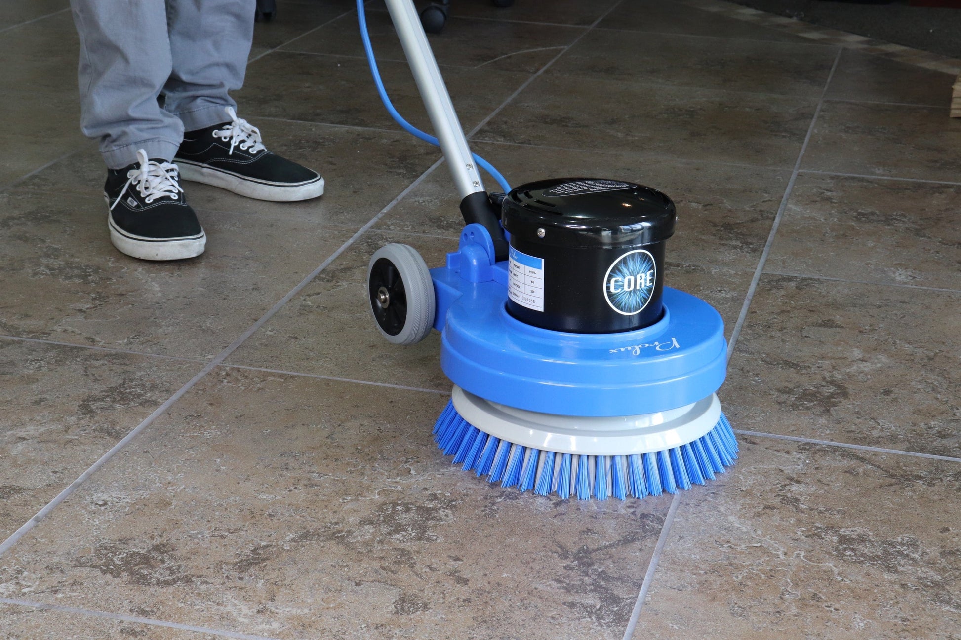 Floor cleaning machine on a tiled floor with a person wearing gray pants and black shoes.